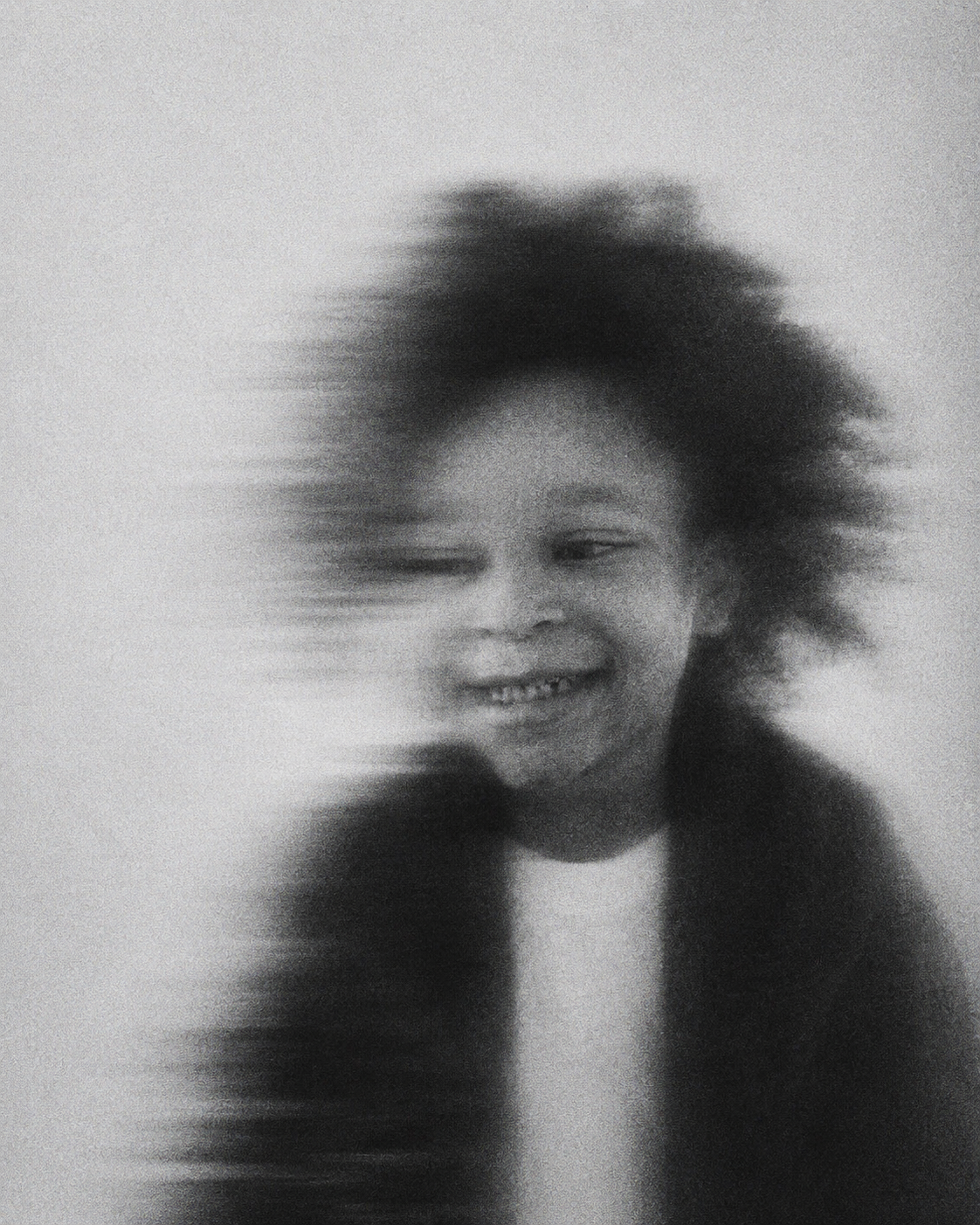 A black and white motion-blur portrait of a smiling child.